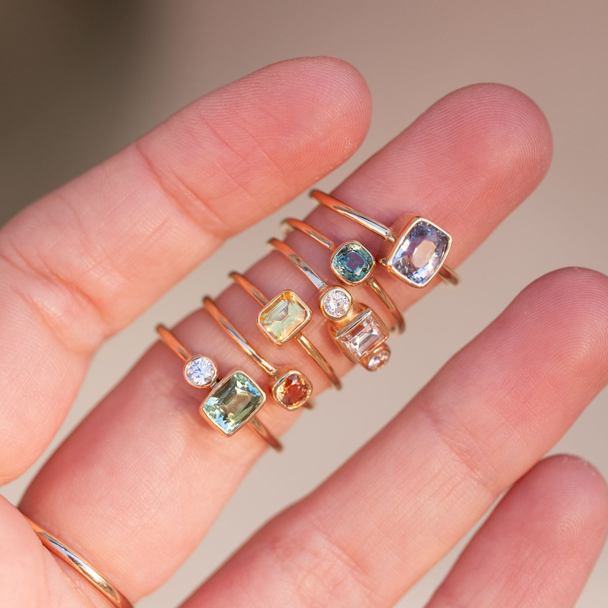 hand showing off multiple gold rings with colorful gemstones and diamonds