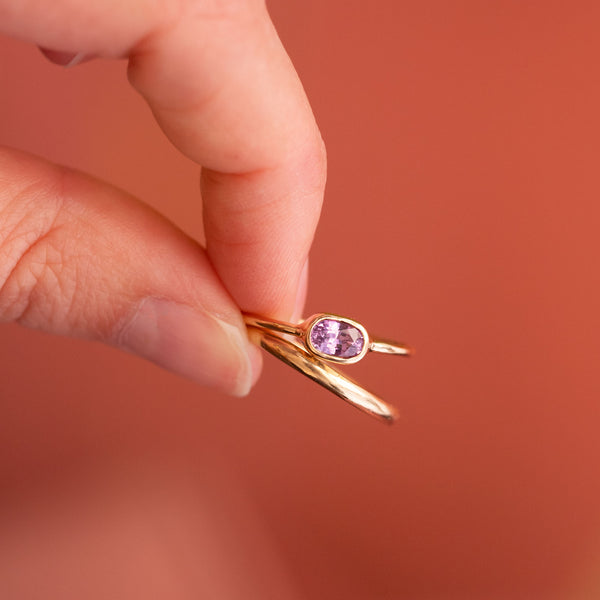 hand holding two 18k gold rings, one plain and one with a pink sapphire