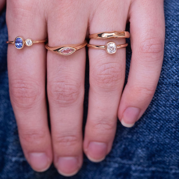 A hand with multiple red gold rings with sapphires and diamonds