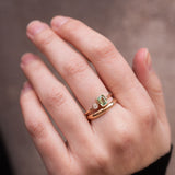 A hand with two gold rings, one plain and one with a green tourmaline and a diamond