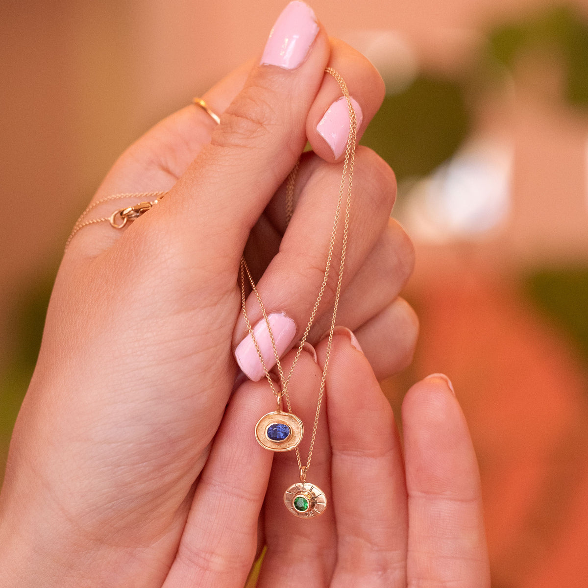 talisman necklces in 18k gold, one with oval blue sapphire and one with round green garnet